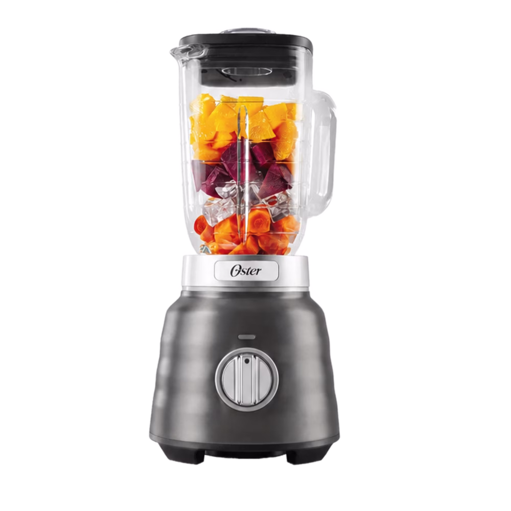 Licuadora Oster BLSTPBRGR negra con vaso de vidrio y frutas en el interior, vista frontal