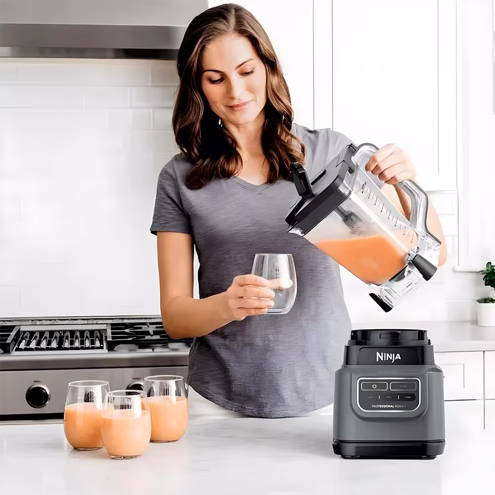 Licuadora Ninja BE200LAA mujer sirviendo batido de naranja en vaso vista frontal. Disponible en granhogar